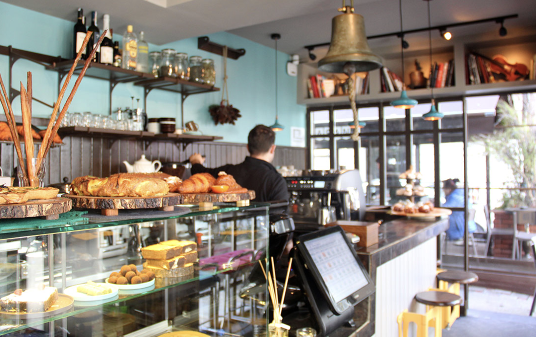 Kafe iç mekanında çeşitli tatlılar, ekmekler ve kahve hazırlayan barista
