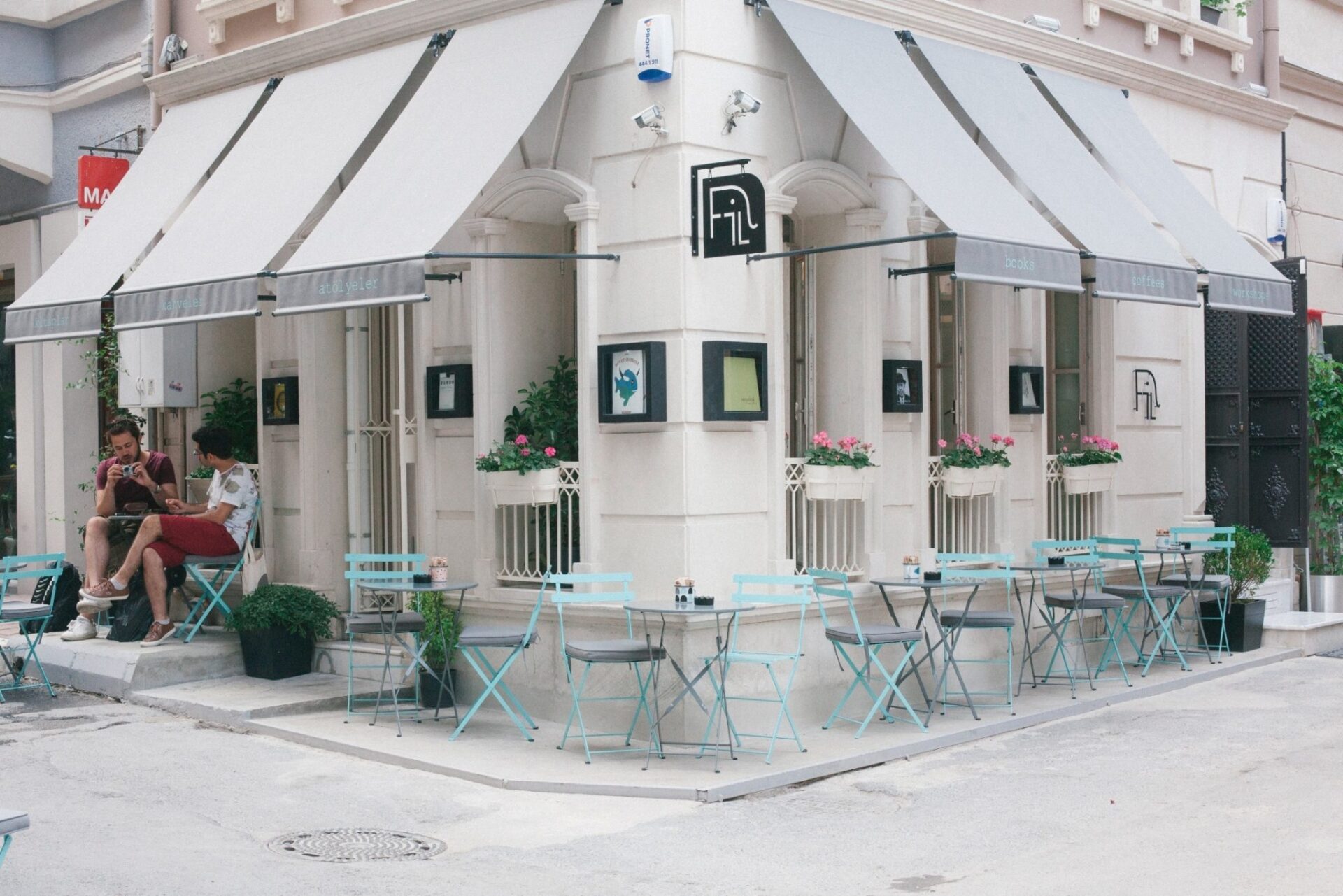Beyaz tenteli köşe kafe, dışarıda oturanlar, turkuaz masalar ve sandalyeler