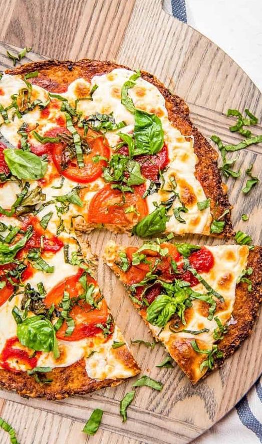 Dilimlenmiş domates mozzarella ve fesleğenli karnabahar pizza ahşap servis tahtasında