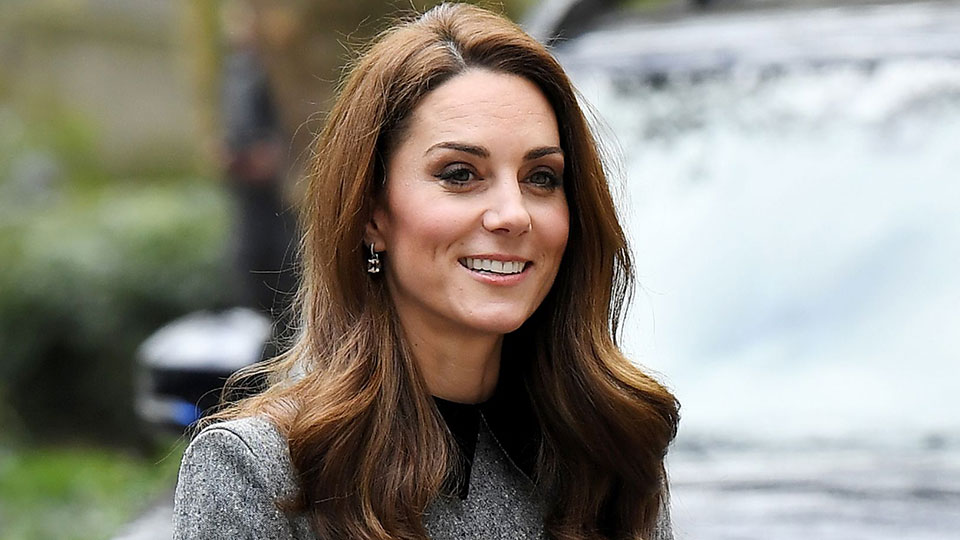 Kate Middleton gülümsüyor uzun kahverengi saçları gri bir palto giymiş