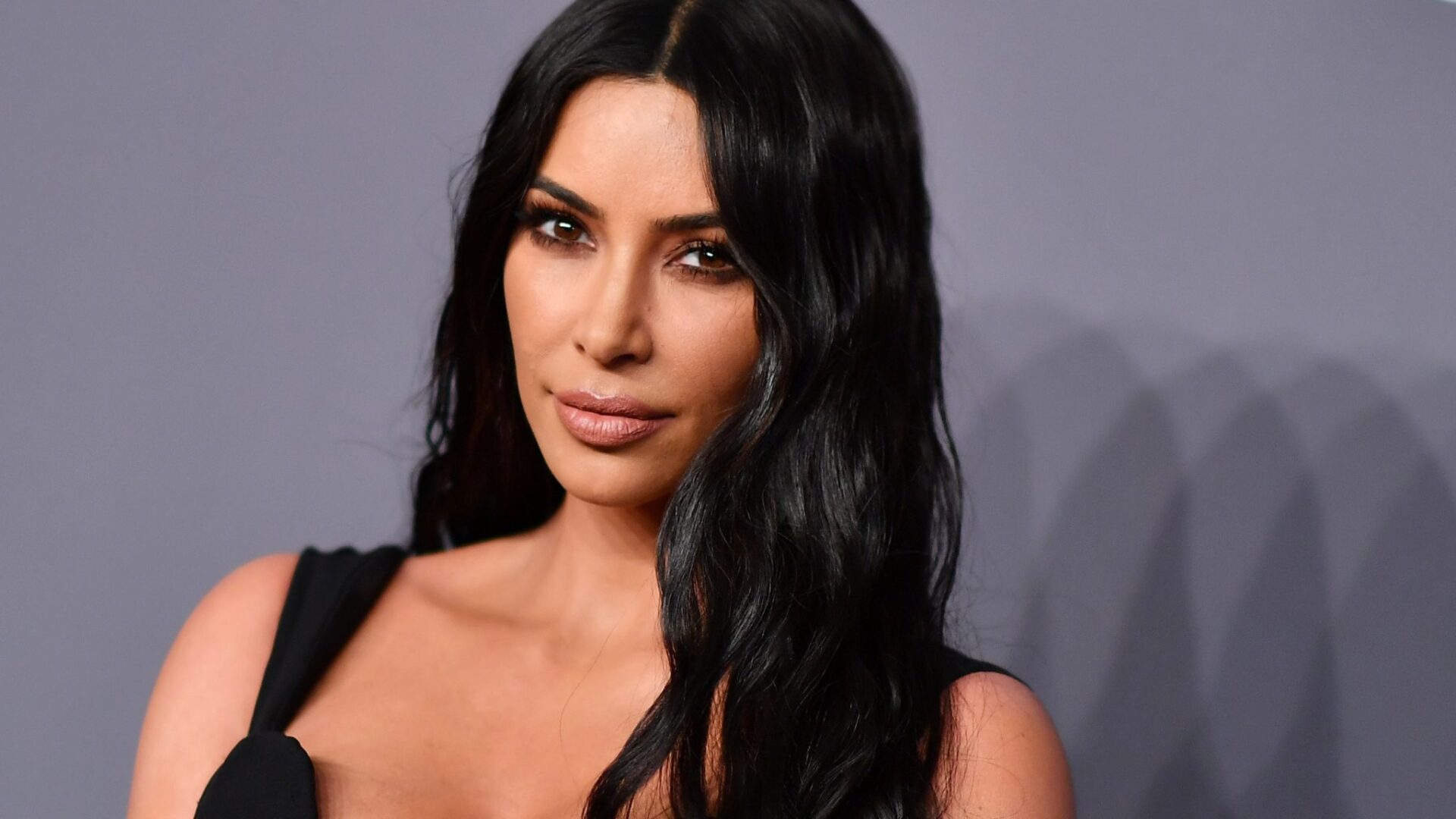 Kim Kardashian koyu dalgalı saçlarıyla siyah elbise içinde kameraya bakıyor
