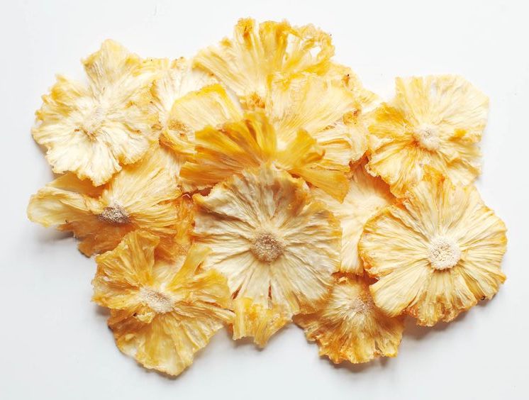 Beyaz fon üzerinde yığılmış parlak sarı kurutulmuş ananas dilimleri