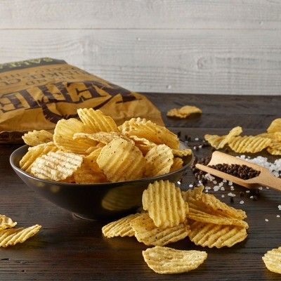 Kıvırcık patates cipsleri kasede, açık paket ve tuz karabiber taneleriyle
