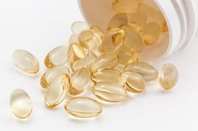 Beyaz şişeden dökülen şeffaf sarı vitamin softgel kapsülleri beyaz zeminde