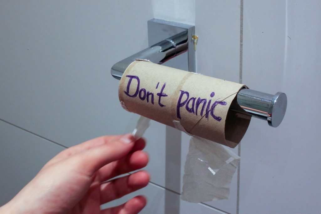 Tuvalet kağıdı bitmiş rulo üzerinde 'Don't Panic' yazısı ve el