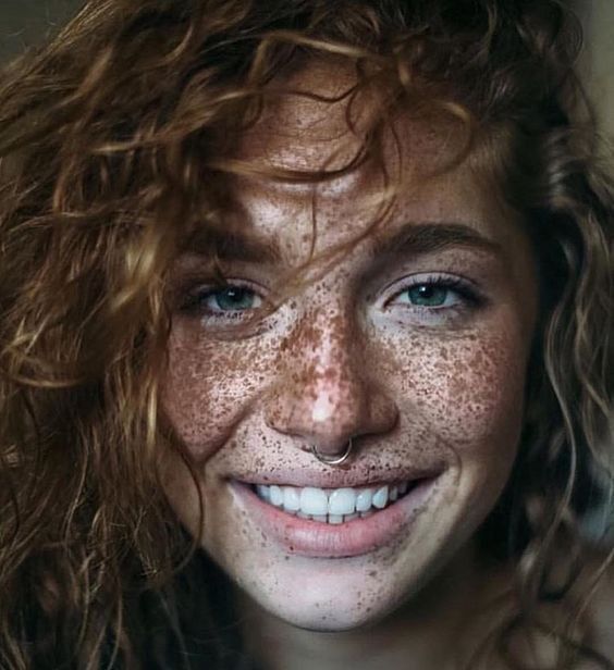 Çilli yüzlü kıvırcık saçlı piercingli gülümseyen genç kadın