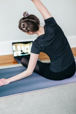 Dizüstü bilgisayardan yoga dersi izleyen kadın matında esniyor