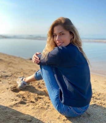 Deniz kenarında kumda oturan gülümseyen sarı saçlı genç kadın