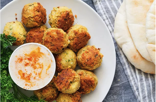 Beyaz tabakta kızarmış falafel köfteleri, sos, maydanoz ve pide ekmeği