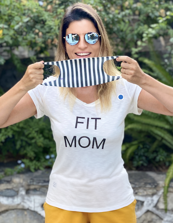 Bir kadın, FIT MOM tişörtü giymiş, çizgili maske tutuyor