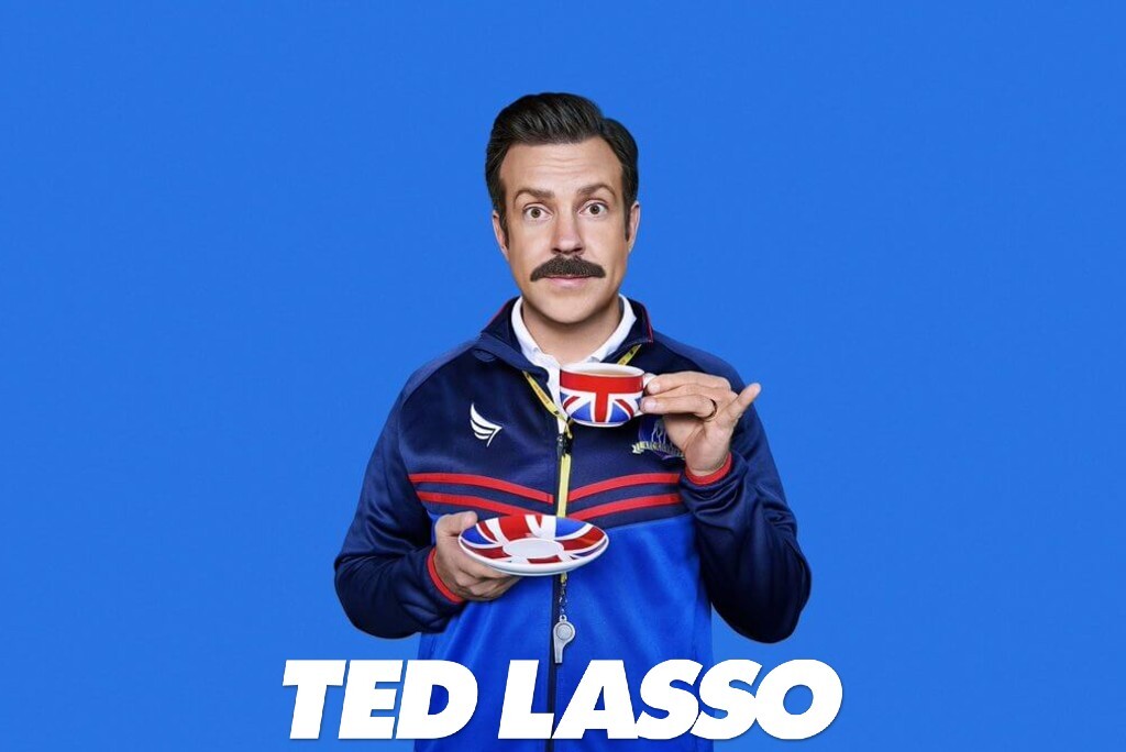 Ted Lasso Union Jack desenli çay fincanı ve tabağı tutuyor mavi arka planda