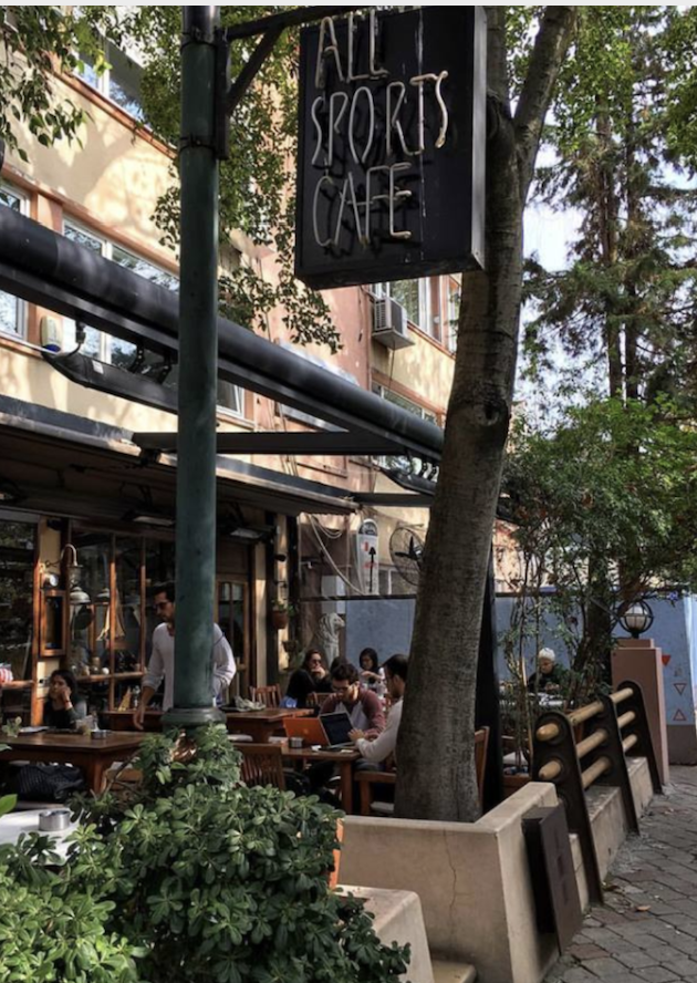 All Sports Cafe'nin açık hava oturma alanında oturan insanlar