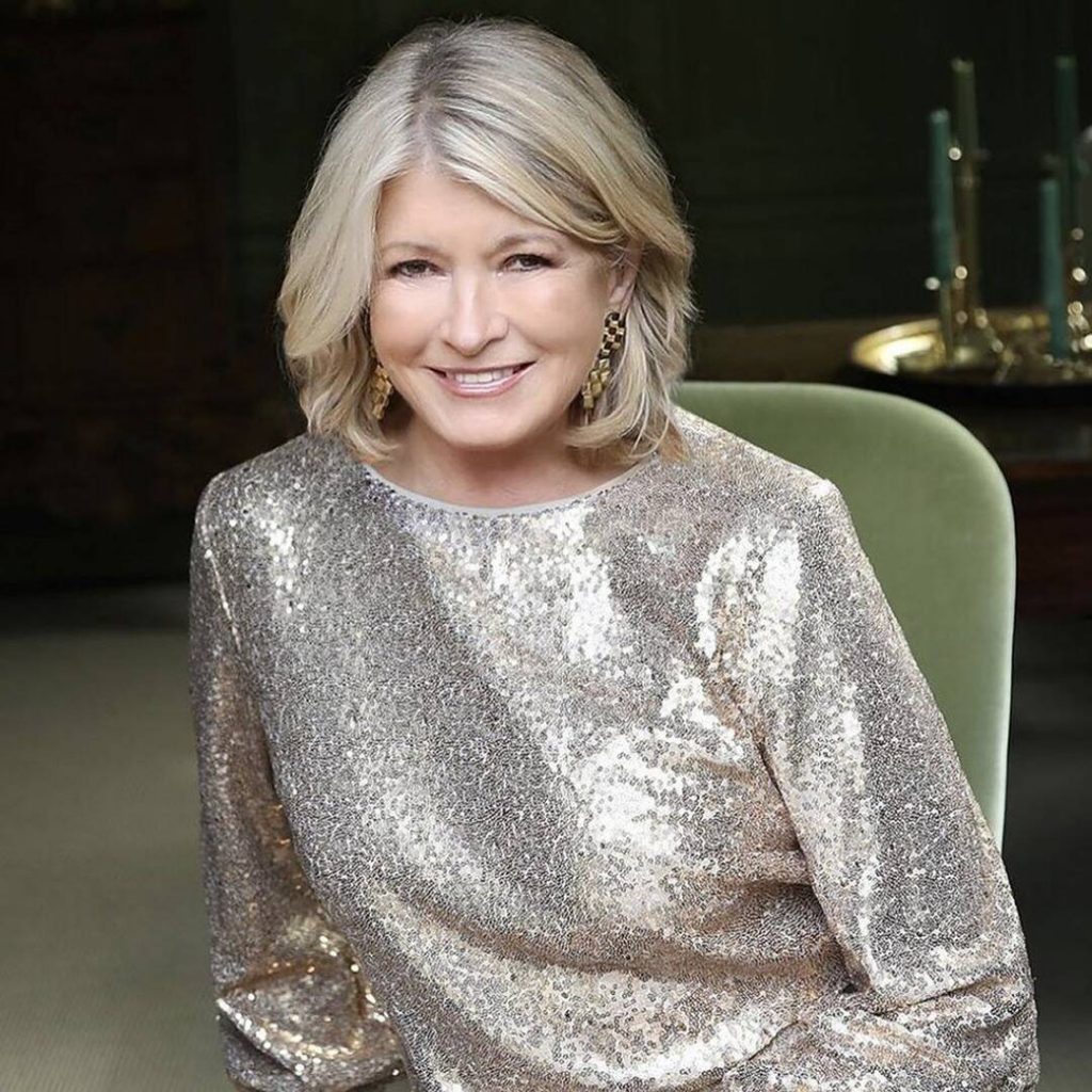 Martha Stewart altın payetli bluzla gülümsüyor yeşil koltukta oturuyor