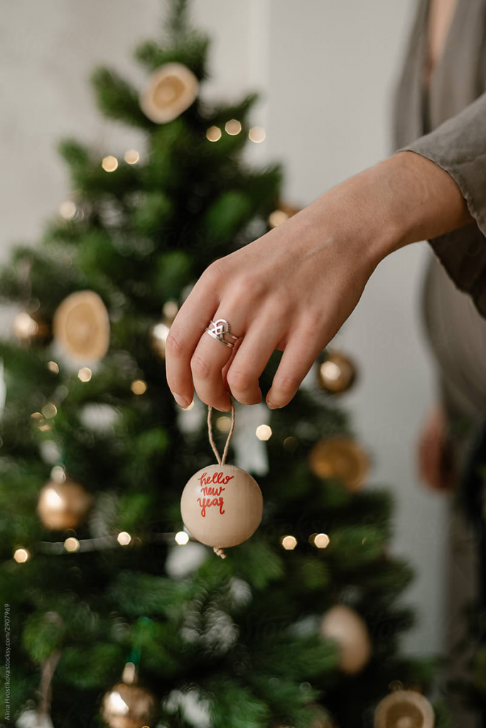 Yılbaşı ağacı önünde elinde üzerinde hello new year yazan süs tutan kadın