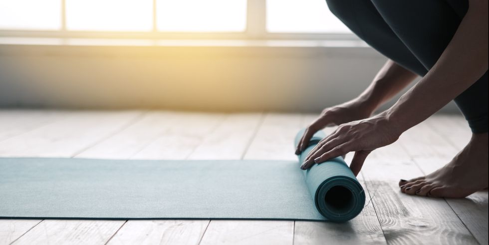 Bir kişi ahşap zeminde mavi yoga matını rulo yapıyor