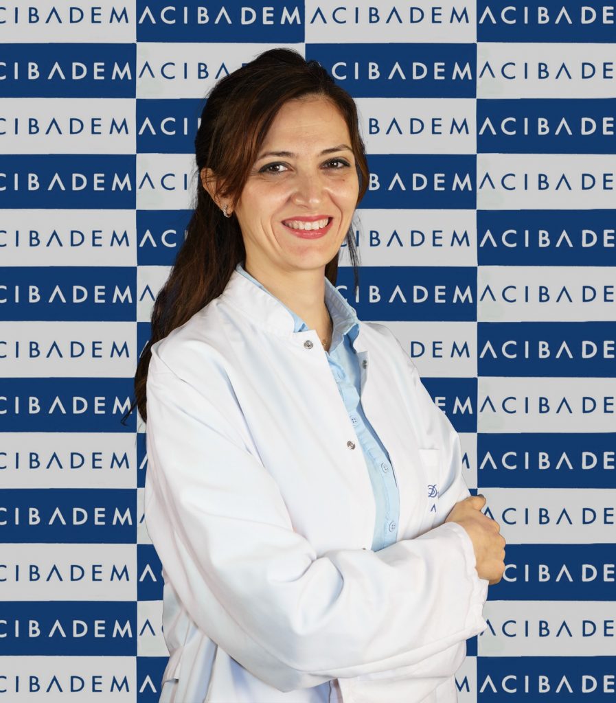 Acıbadem logosu önünde kolları bağlı, gülümseyen bir kadın doktor