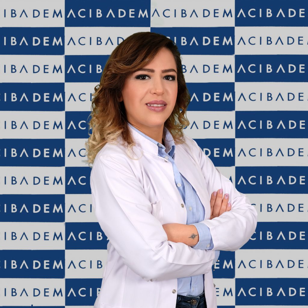 Acıbadem logolu arka planda, beyaz önlüklü gülümseyen kadın doktor portresi