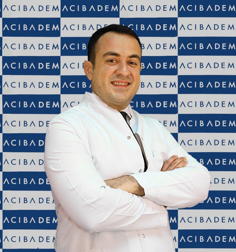 Acıbadem logosu önünde beyaz önlüklü gülümseyen erkek doktor
