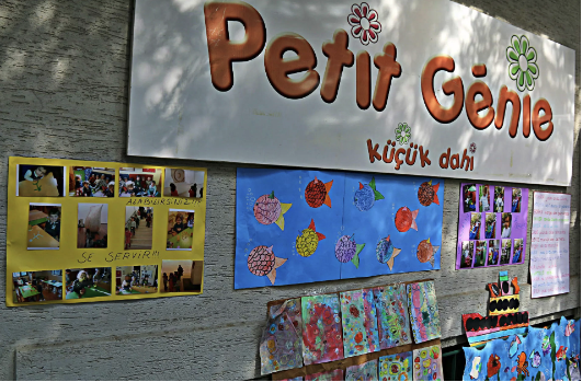 Çocuk sanat eserleri ve etkinlik fotoğraflarıyla süslenmiş Petit Génie anaokulu duvarı