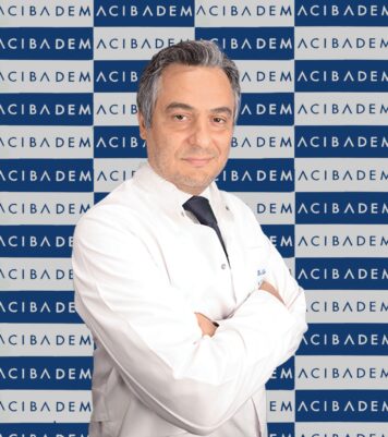 Acıbadem logolu arka planda beyaz önlüklü gülümseyen erkek doktor