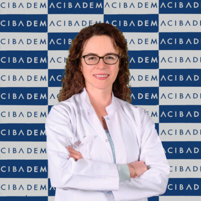 Acıbadem logosu önünde beyaz önlüklü gülümseyen gözlüklü kadın doktor