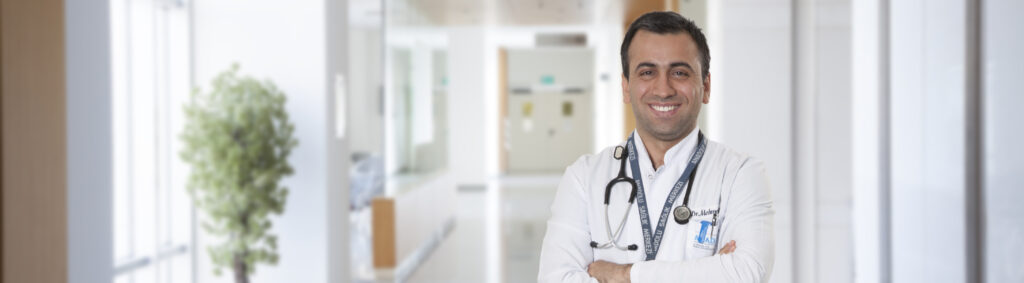 Gülümseyen beyaz önlüklü erkek doktor hastane koridorunda steteskopuyla