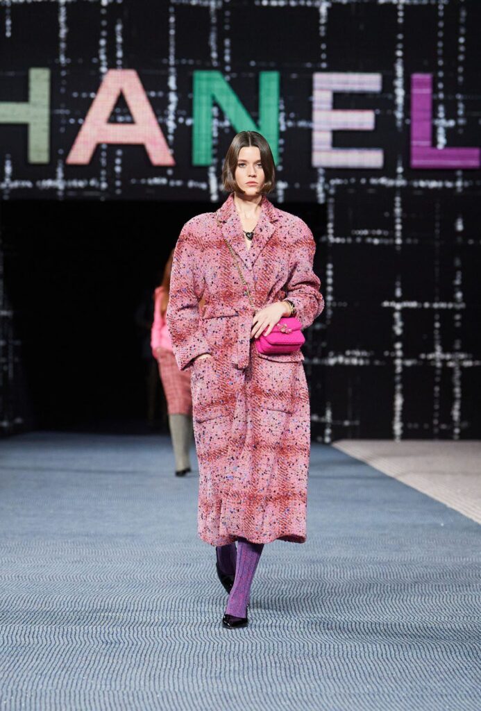 Model pembe tüvit palto, pembe çanta ve mor çoraplarla Chanel podyumunda yürüyor