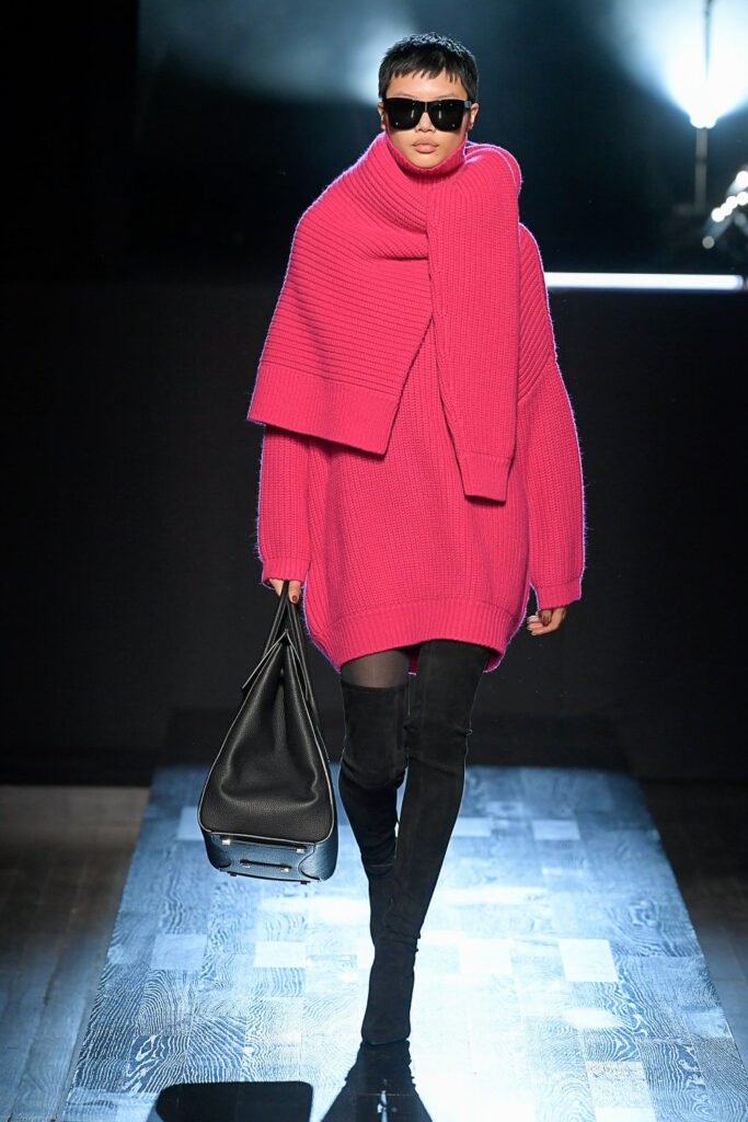 Pembe oversized kazak, siyah çizme ve çanta giymiş model podyumda