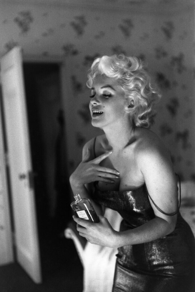 Marilyn Monroe gülümserken elinde parfümle ayna karşısında