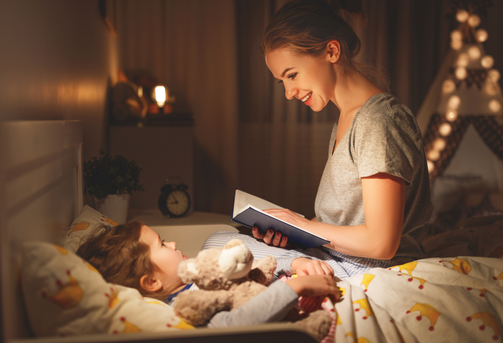 Anne ve kızı yatakta gülümseyerek gece masalı okuyorlar
