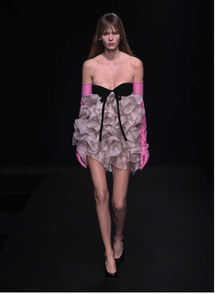Model pembe eldivenli, fırfırlı etekli askısız elbisesiyle podyumda