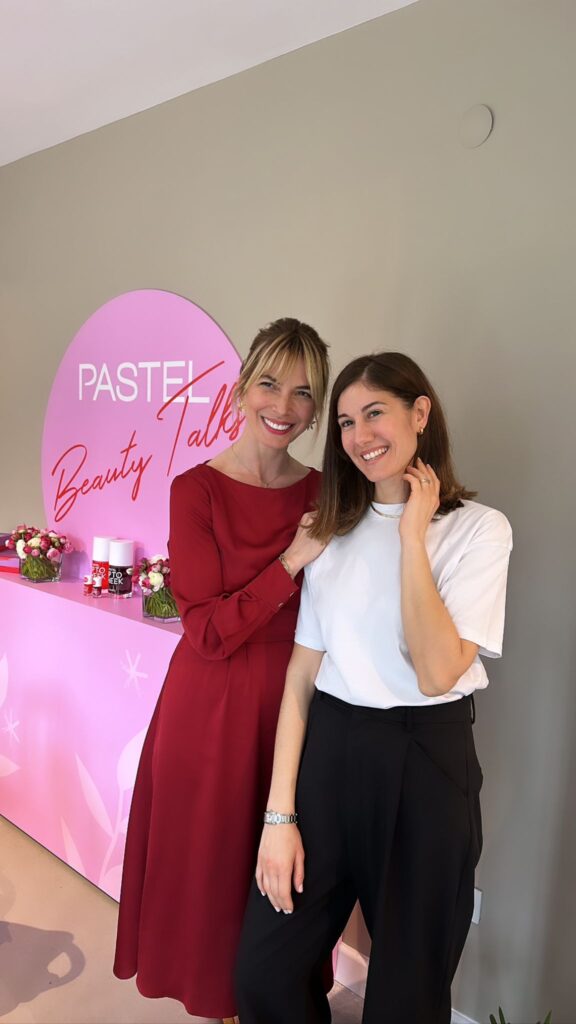Pastel Beauty Talks panosu önünde gülümseyen iki kadın
