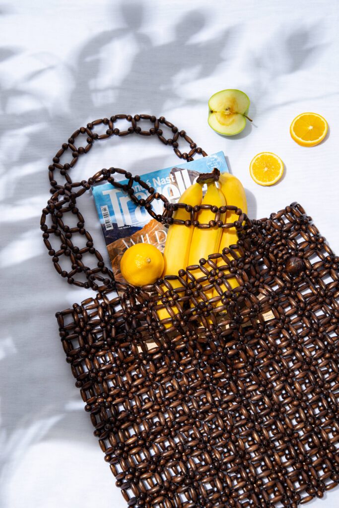 Ahşap boncuklu çanta içinde muz limon elma portakal ve dergi