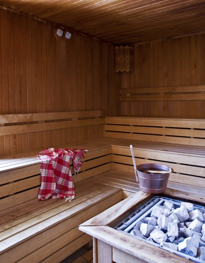 Ahşap sauna iç mekanı, banklar, kırmızı havlu, kova ve ısıtıcı taşları