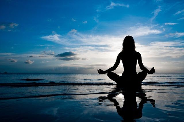 Gün batımında sahilde yoga yapan kadın silueti ve yansıması