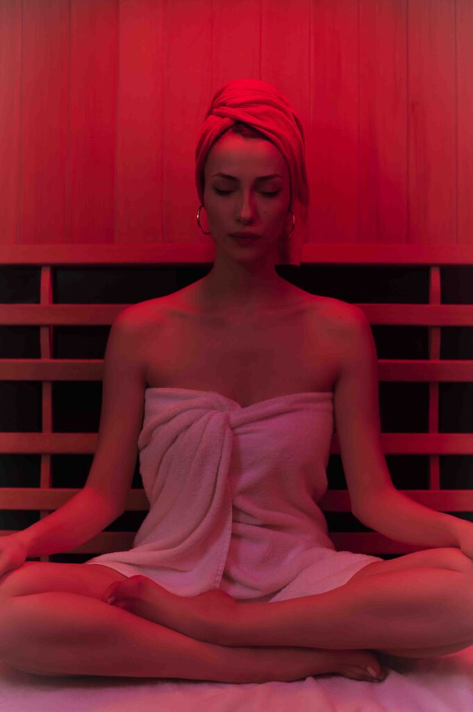 Kırmızı ışıklı saunada gözleri kapalı meditasyon yapan havlulu kadın