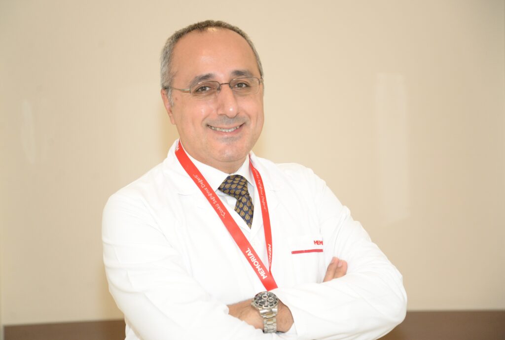 Beyaz önlüklü gülümseyen erkek doktor kırmızı MEMORIAL yaka kartı takıyor