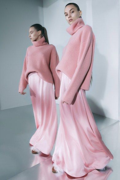 İki model pembe kazak ve saten etekleriyle yansımalı bir ortamda duruyor