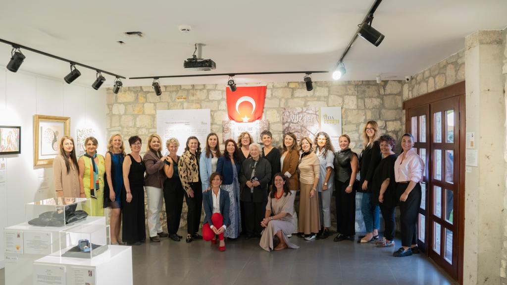 Bir sanat galerisinde Türk bayrağı önünde poz veren gülümseyen kadınlar grubu