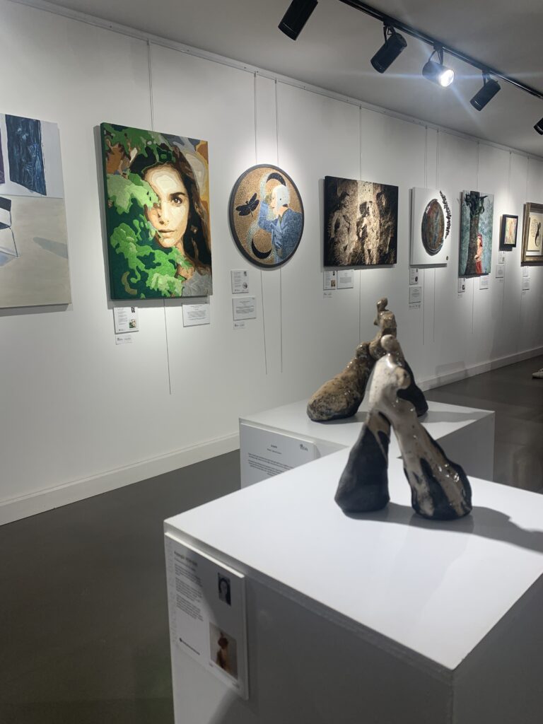Sanat galerisinde beyaz duvarlarda asılı çeşitli tablolar ve modern heykeller