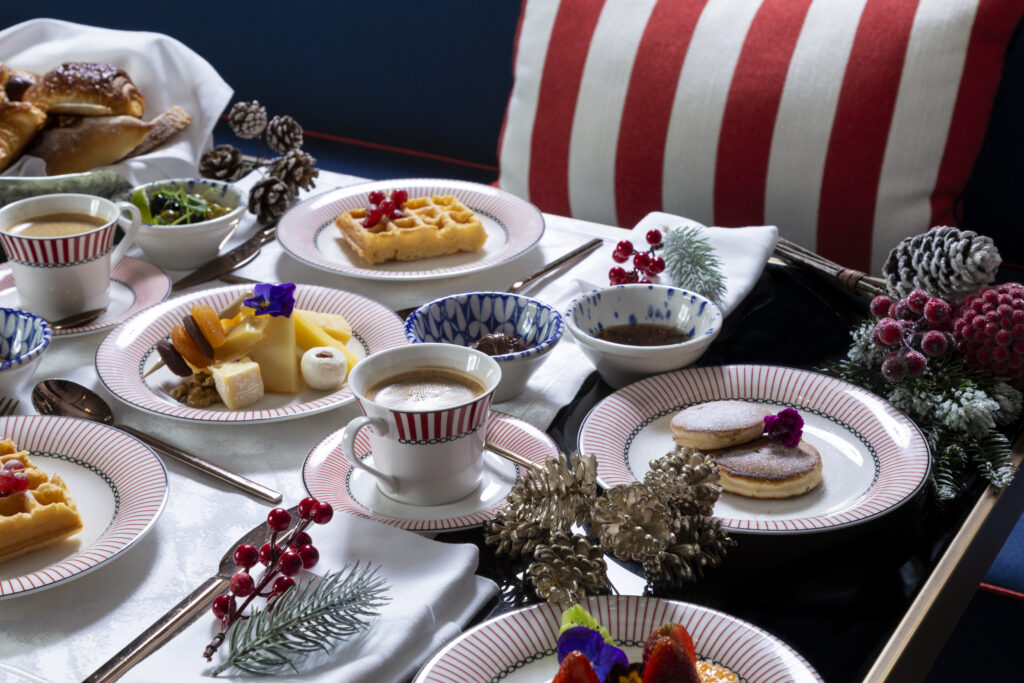 Kırmızı şeritli tabaklarda waffle krep kahve ve Noel dekorasyonları içeren kahvaltı