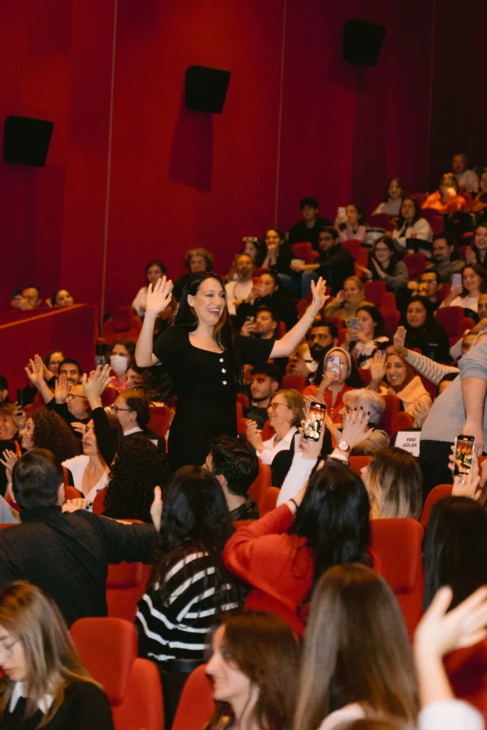 Sinema salonunda siyah elbiseli kadın alkışlayan seyirciye el sallıyor