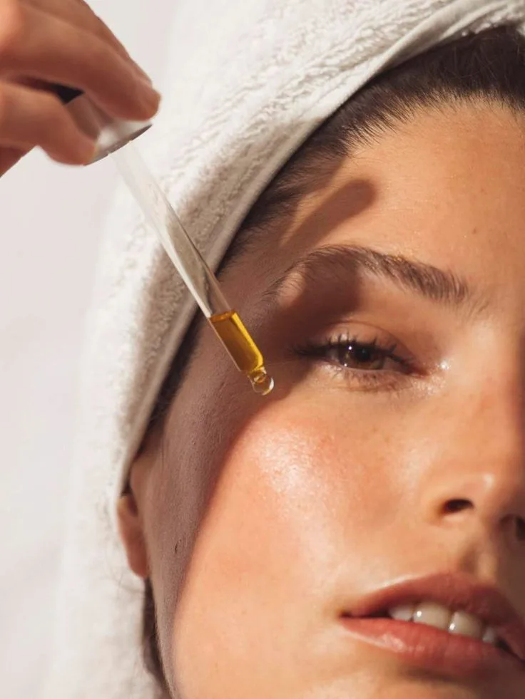 Havlu takmış kadın yüzüne damlatıcı ile serum veya yağ uyguluyor