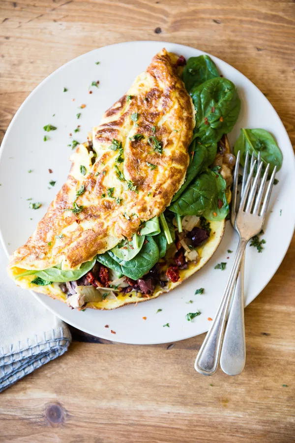 Beyaz tabakta otlu ıspanak güneş kurusu domates ve zeytinli omlet