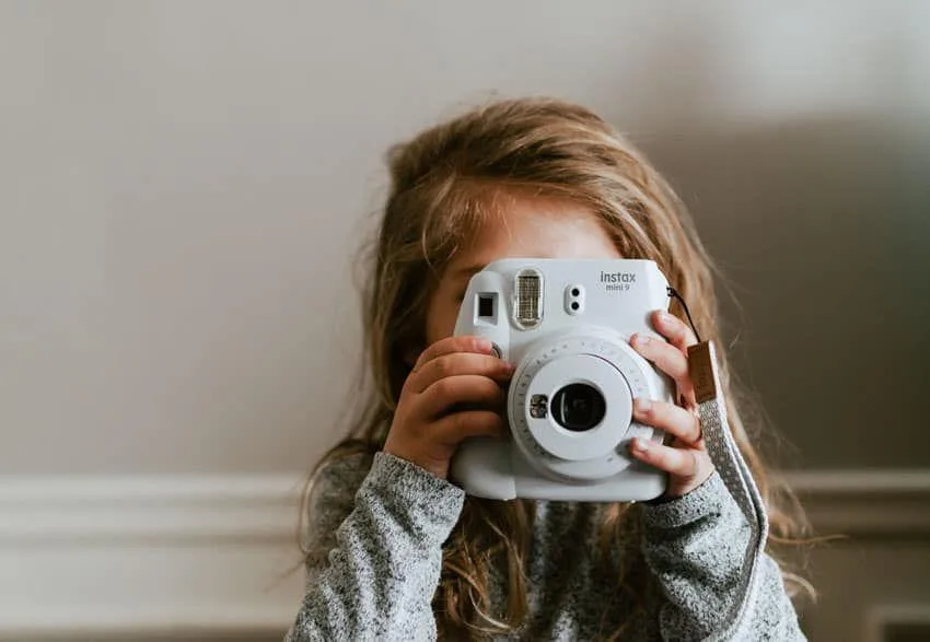 Kız çocuğu beyaz Instax Mini 9 fotoğraf makinesiyle fotoğraf çekiyor