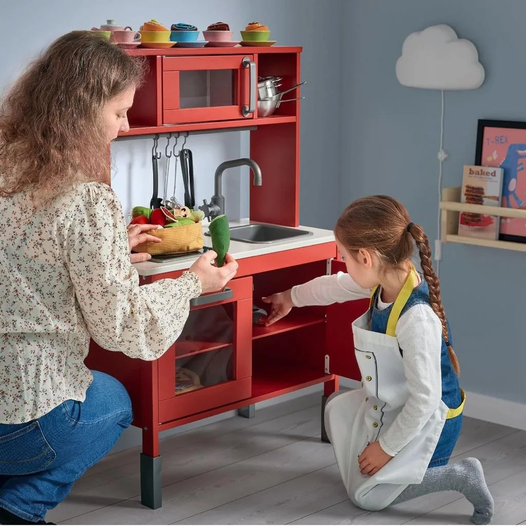 Anne ve kızı kırmızı oyuncak mutfakta sebzelerle oynuyor