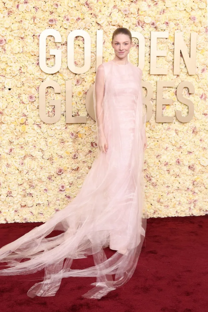 Kırmızı halıda şeffaf pembe elbise giyen kadın Golden Globes logosu önünde