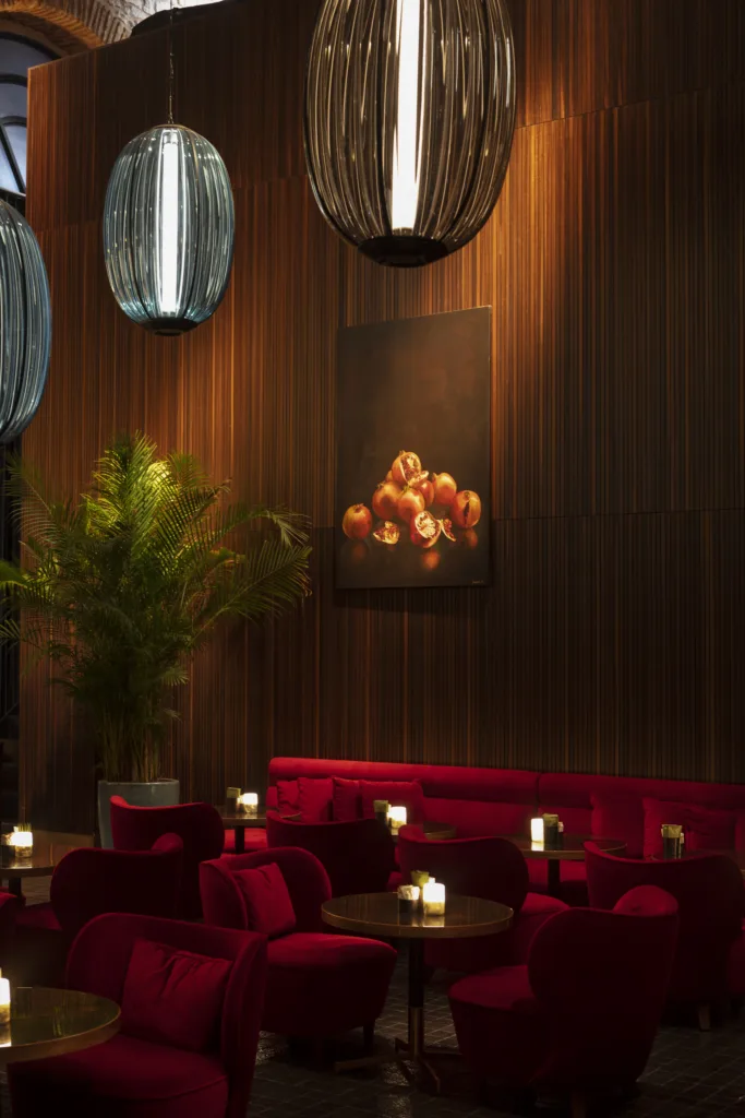 Kırmızı koltuklu, ahşap duvarlı, modern avizeli ve bitkili loş bir bar