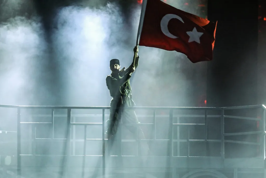 Dumanlı sahnede Türk bayrağı kaldıran siluet bir figür