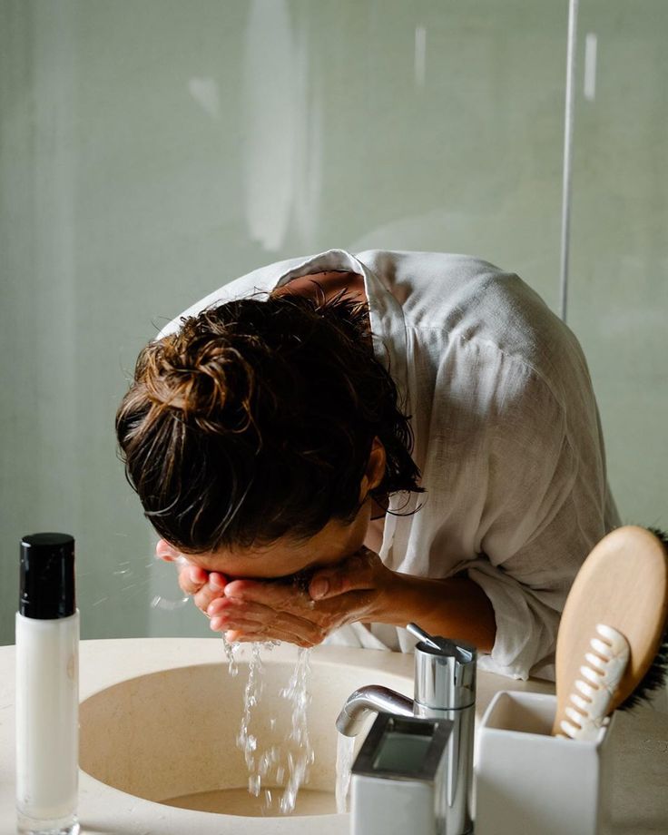 Lavaboda yüzünü yıkayan bir kişi banyo ortamında